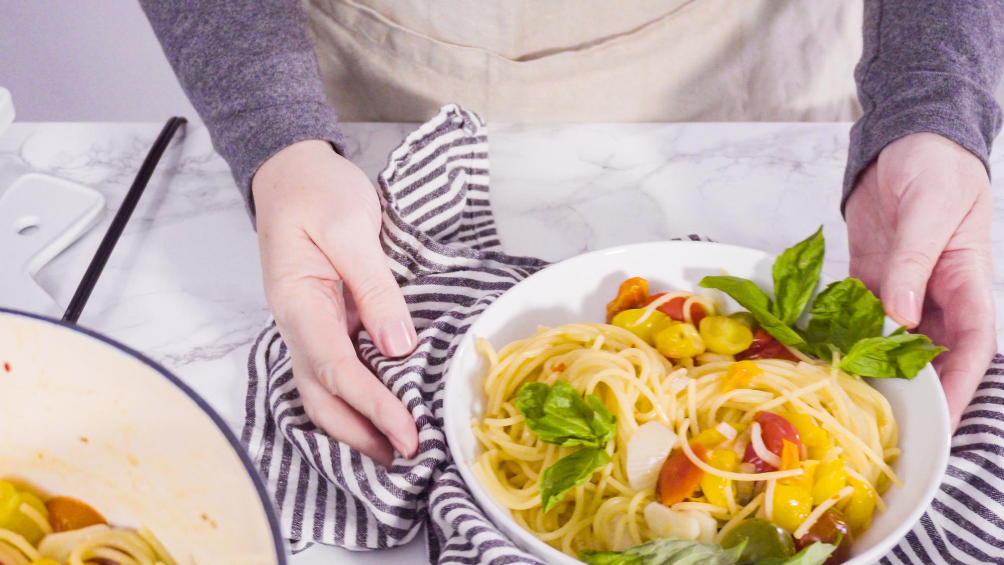 Hands plating a simple pasta in a bright kitchen